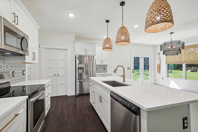 kitchen featuring a center island with sink, sink, backsplash, white cabinets, and appliances with stainless steel finishes