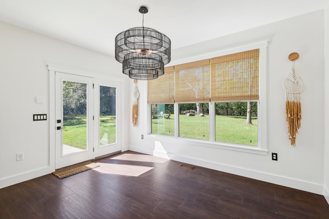 unfurnished dining area featuring an inviting chandelier, plenty of natural light, and dark hardwood / wood-style flooring