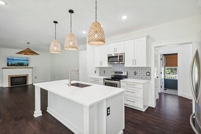 kitchen with an island with sink, stainless steel appliances, sink, white cabinetry, and decorative light fixtures