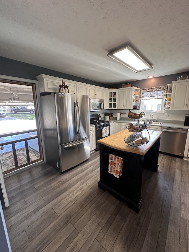 kitchen featuring appliances with stainless steel finishes, dark hardwood / wood-style flooring, a textured ceiling, white cabinets, and a kitchen island