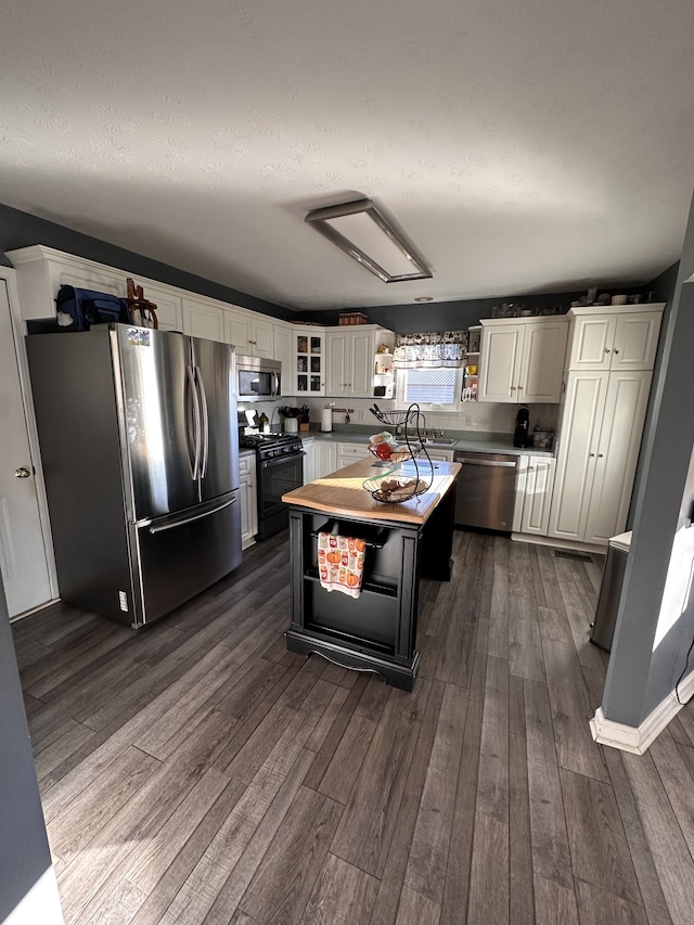 kitchen with white cabinetry, stainless steel appliances, dark hardwood / wood-style floors, a textured ceiling, and a kitchen island