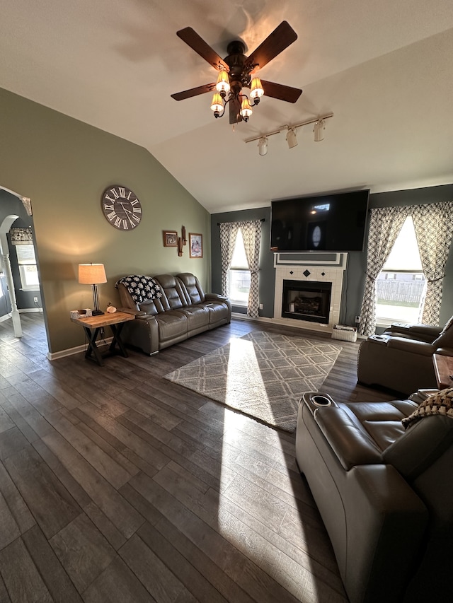 living room with a tile fireplace, ceiling fan, dark wood-type flooring, and vaulted ceiling