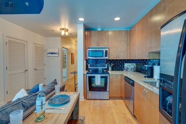 kitchen featuring light hardwood / wood-style floors, sink, light stone countertops, backsplash, and appliances with stainless steel finishes