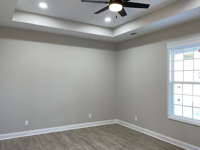 unfurnished room with ceiling fan, dark wood-type flooring, and a tray ceiling