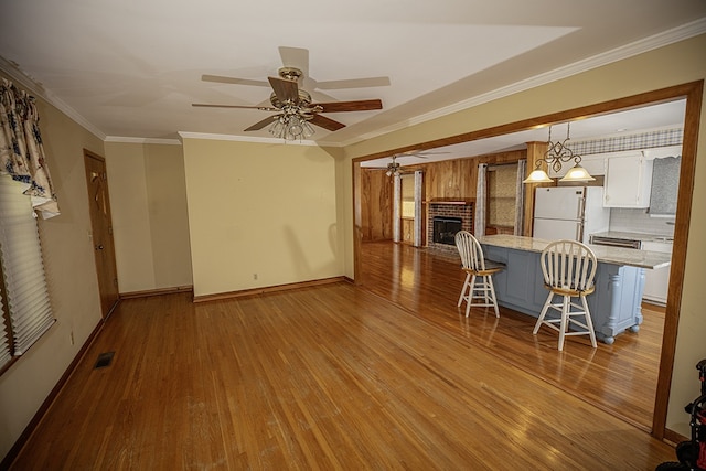 interior space featuring ceiling fan with notable chandelier, ornamental molding, a fireplace, and light hardwood / wood-style flooring