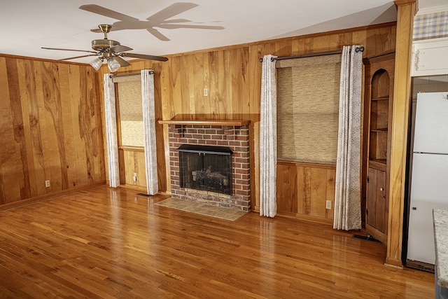 unfurnished living room featuring a fireplace, hardwood / wood-style flooring, ceiling fan, and wooden walls