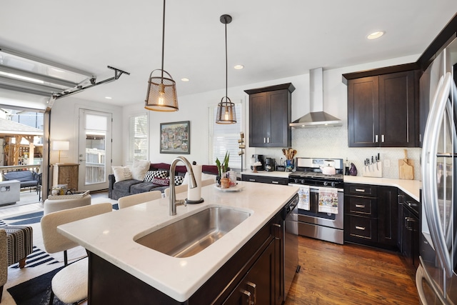 kitchen featuring hanging light fixtures, a center island with sink, wall chimney range hood, stainless steel appliances, and dark hardwood / wood-style floors