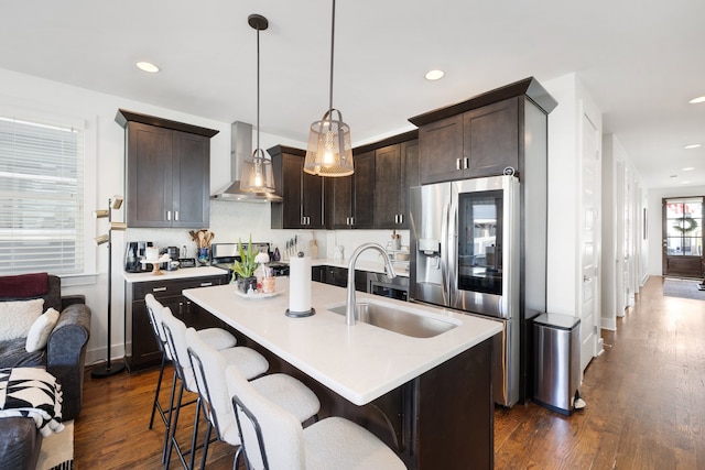 kitchen with sink, dark hardwood / wood-style flooring, pendant lighting, wall chimney range hood, and stainless steel fridge with ice dispenser