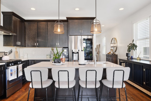 kitchen with wall chimney exhaust hood, dark hardwood / wood-style floors, appliances with stainless steel finishes, and a kitchen island with sink