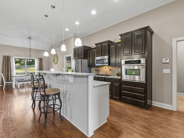 kitchen featuring an island with sink, decorative light fixtures, dark wood-type flooring, appliances with stainless steel finishes, and a kitchen bar