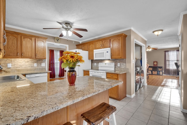 kitchen with white appliances, washing machine and clothes dryer, crown molding, kitchen peninsula, and a kitchen bar