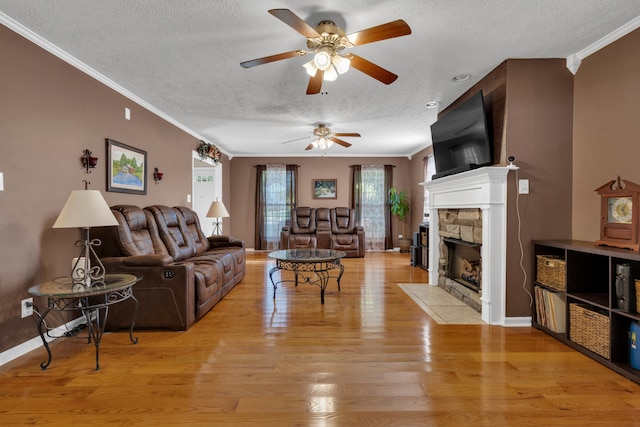 living room featuring a stone fireplace, a textured ceiling, crown molding, and light hardwood / wood-style floors