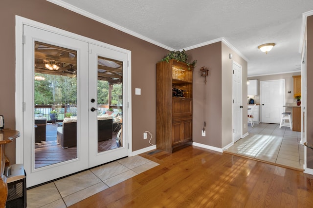 entryway with ornamental molding, light wood-type flooring, french doors, and a textured ceiling