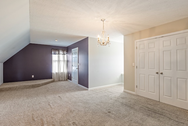 spare room with a notable chandelier, carpet floors, a textured ceiling, and vaulted ceiling