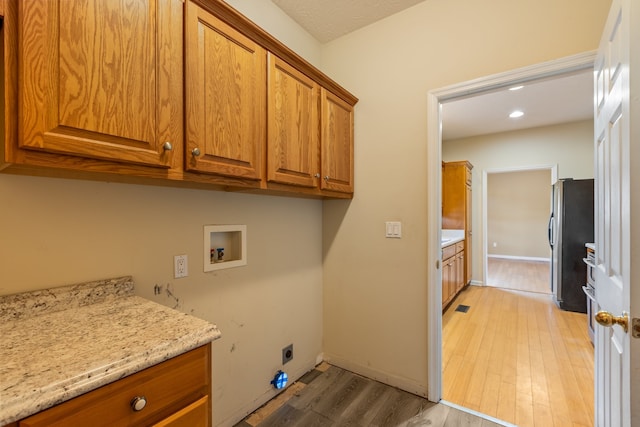 clothes washing area featuring cabinets, light hardwood / wood-style flooring, washer hookup, and electric dryer hookup