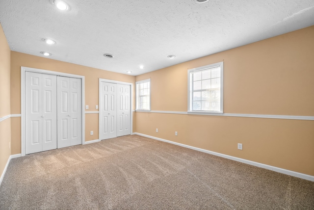 unfurnished bedroom featuring a textured ceiling, two closets, and carpet floors