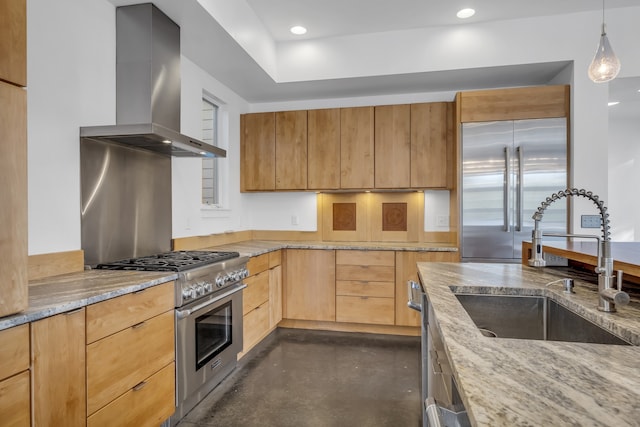 kitchen with sink, wall chimney range hood, light stone counters, and high end appliances