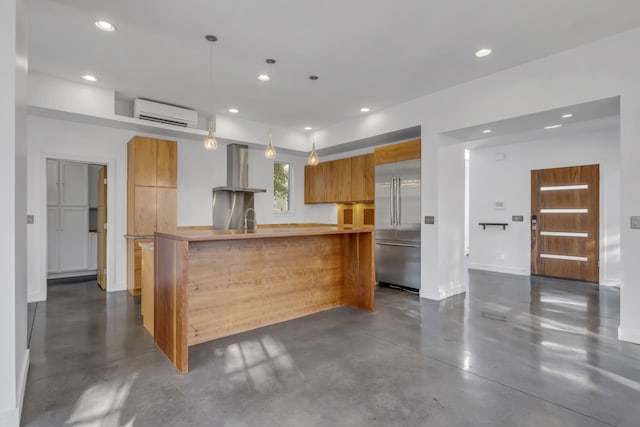 kitchen with stainless steel built in fridge, pendant lighting, sink, wall chimney exhaust hood, and a wall mounted air conditioner