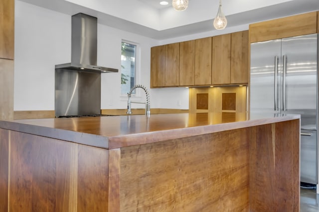 kitchen featuring stainless steel built in refrigerator, wall chimney exhaust hood, sink, and decorative light fixtures