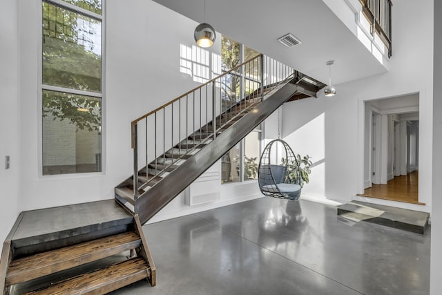 stairs featuring concrete flooring, a towering ceiling, and a healthy amount of sunlight