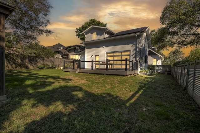 back house at dusk featuring a deck and a lawn