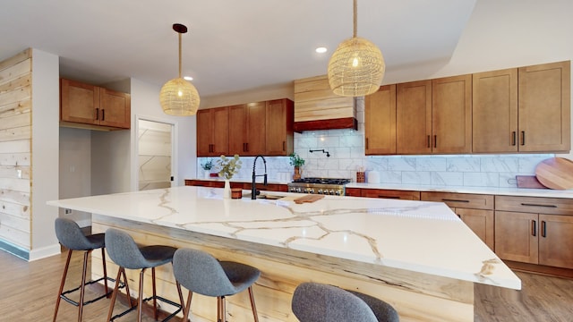 kitchen featuring a center island with sink, hanging light fixtures, custom range hood, and light hardwood / wood-style flooring