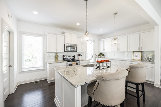 kitchen featuring stainless steel appliances, a breakfast bar, white cabinets, sink, and a center island with sink