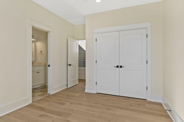 unfurnished bedroom featuring a closet, connected bathroom, and light hardwood / wood-style flooring