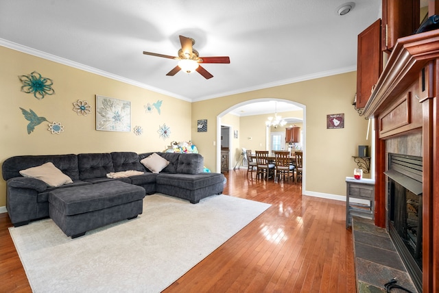 living room featuring hardwood / wood-style flooring, ceiling fan with notable chandelier, a tiled fireplace, and crown molding