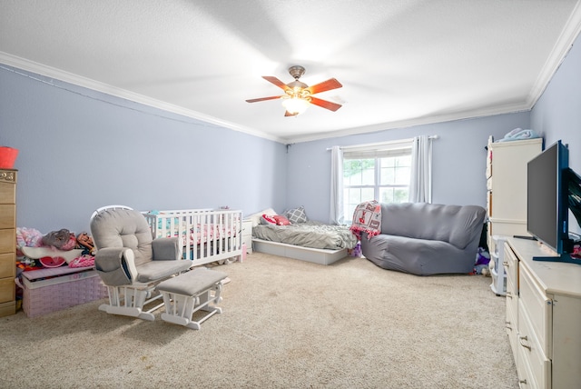 carpeted bedroom with a nursery area, ornamental molding, and ceiling fan