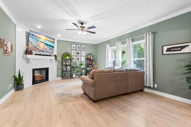 living room featuring a textured ceiling, light wood-type flooring, ornamental molding, and a large fireplace