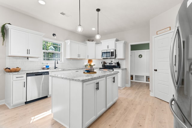 kitchen featuring a center island, stainless steel appliances, white cabinets, hanging light fixtures, and light hardwood / wood-style flooring