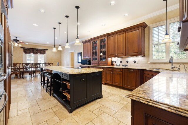 kitchen featuring crown molding, sink, light stone countertops, hanging light fixtures, and a center island