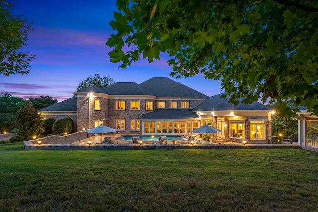 back house at dusk featuring a lawn and a patio area