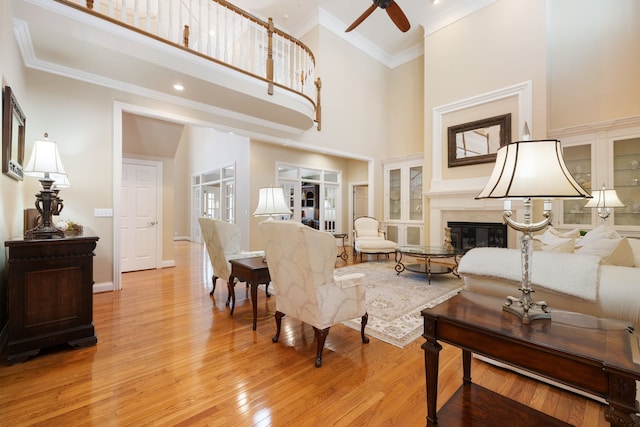 living room with ornamental molding, ceiling fan, a towering ceiling, and light hardwood / wood-style floors