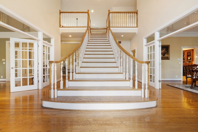 stairs with ornamental molding, a towering ceiling, and wood-type flooring