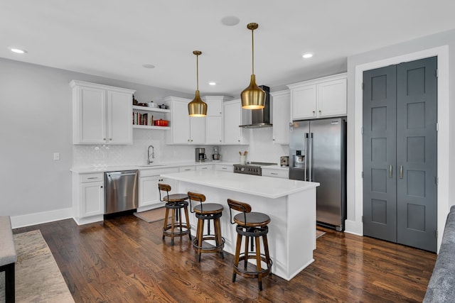 kitchen featuring premium appliances, pendant lighting, white cabinets, and wall chimney range hood