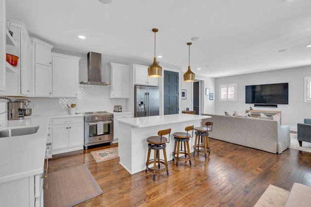 kitchen with white cabinets, wall chimney exhaust hood, stainless steel appliances, dark hardwood / wood-style floors, and a center island