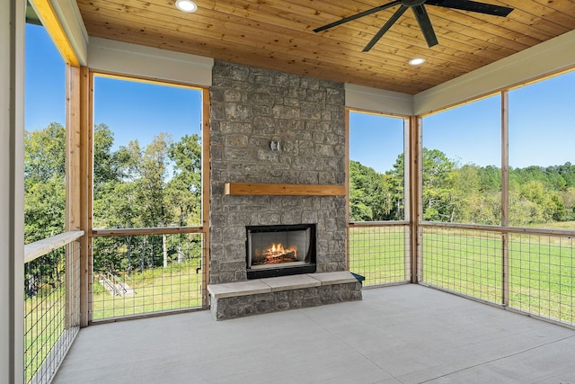 unfurnished sunroom featuring a healthy amount of sunlight, ceiling fan, a fireplace, and wood ceiling