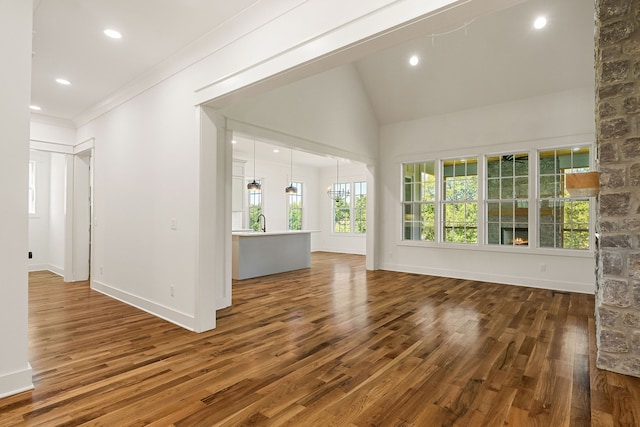 unfurnished living room with high vaulted ceiling, dark wood-type flooring, sink, crown molding, and a chandelier