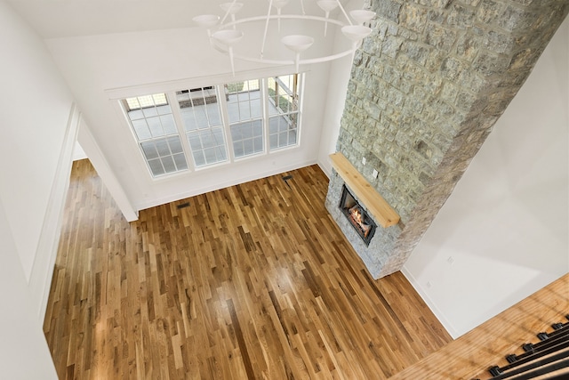 unfurnished living room with an inviting chandelier, hardwood / wood-style flooring, a fireplace, and high vaulted ceiling