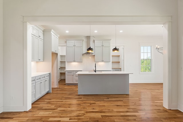 kitchen with pendant lighting, an island with sink, sink, light hardwood / wood-style flooring, and wall chimney range hood