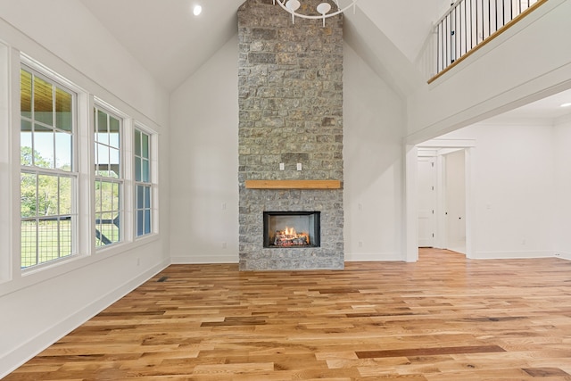 unfurnished living room with high vaulted ceiling, light hardwood / wood-style flooring, and a stone fireplace