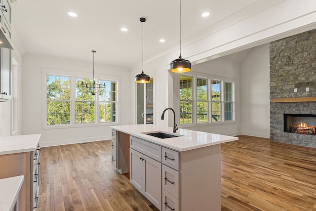 kitchen featuring sink, decorative light fixtures, a center island with sink, a fireplace, and light wood-type flooring