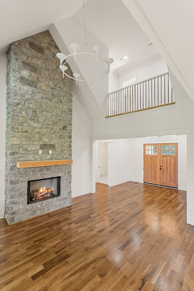 unfurnished living room featuring high vaulted ceiling, a chandelier, a stone fireplace, and wood-type flooring