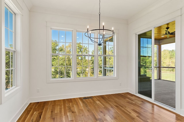 unfurnished dining area with ornamental molding, hardwood / wood-style flooring, plenty of natural light, and ceiling fan with notable chandelier