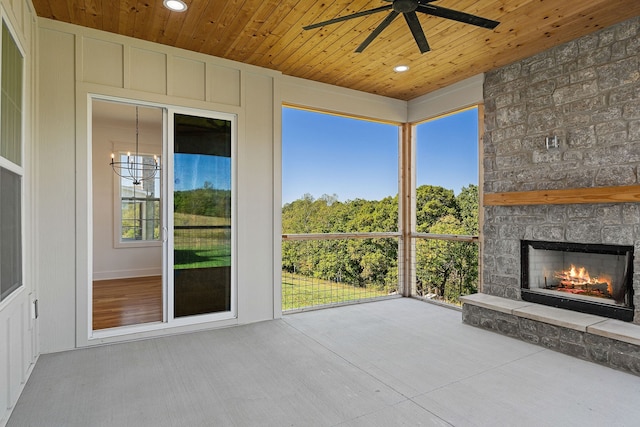 unfurnished sunroom with ceiling fan with notable chandelier, a stone fireplace, and wood ceiling