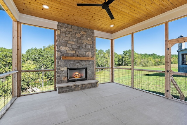 unfurnished sunroom with ceiling fan, a fireplace, plenty of natural light, and wooden ceiling