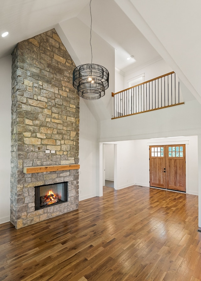 unfurnished living room featuring high vaulted ceiling, hardwood / wood-style floors, a notable chandelier, and a stone fireplace