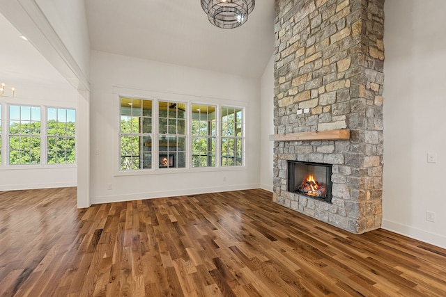 unfurnished living room featuring hardwood / wood-style flooring, high vaulted ceiling, plenty of natural light, and a stone fireplace